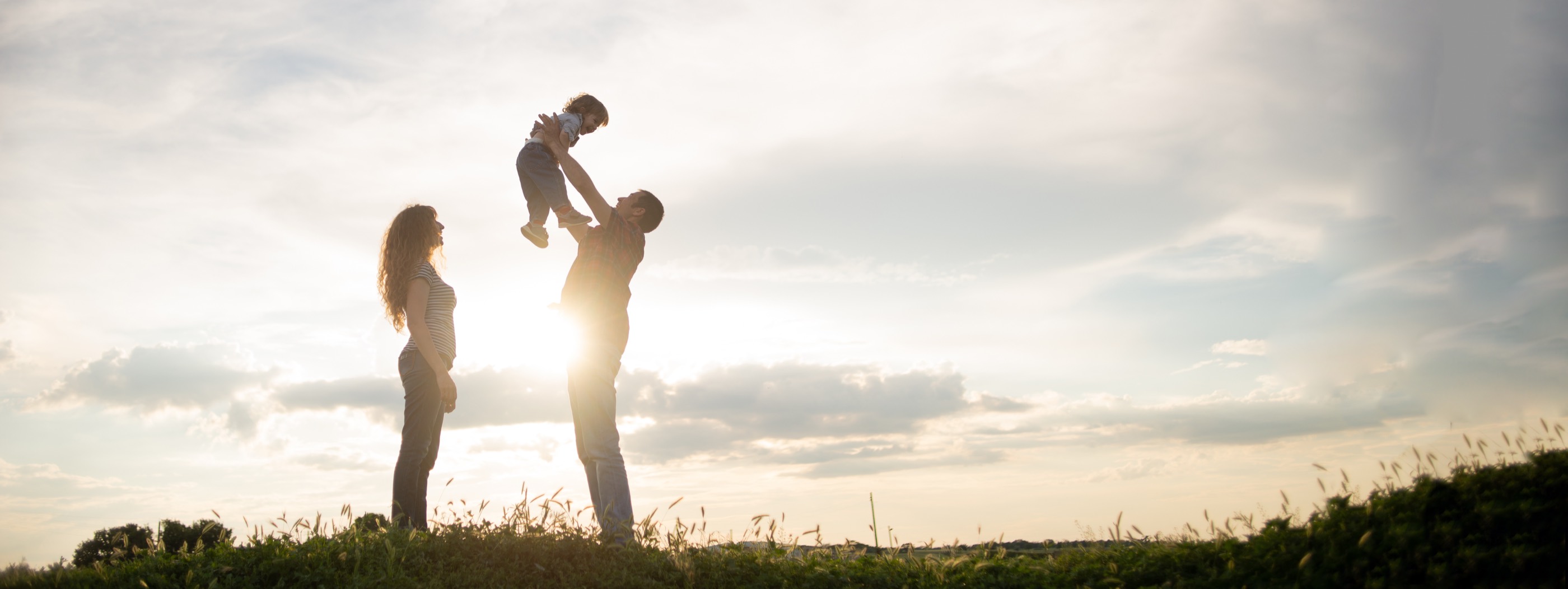 Two adults lifting a small child on a ridge against an open sky.